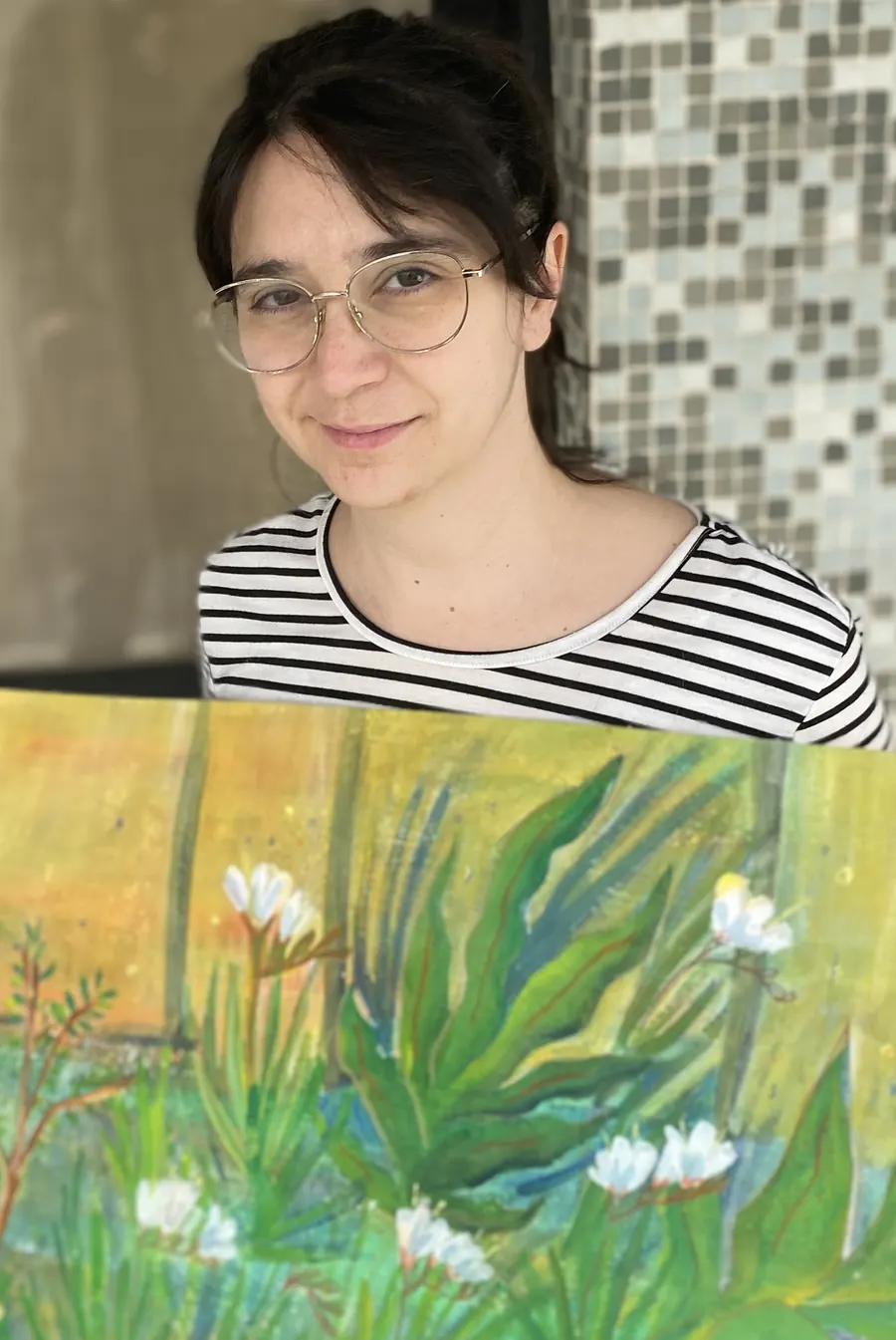 Nat sonriendo detrás de un cuadro suyo: hojas verdes y flores blancas sobre un fondo amarillo.